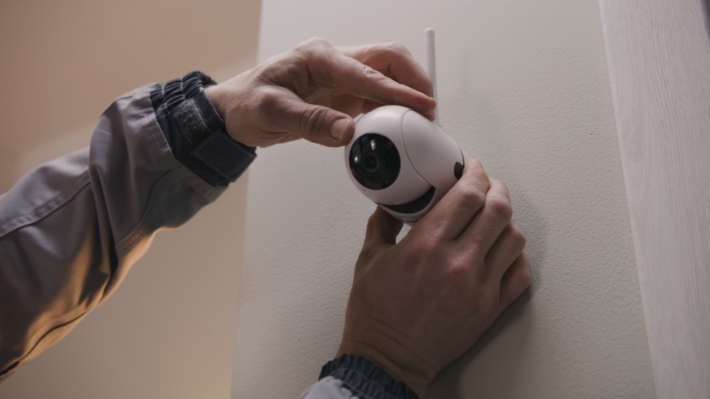 Installer In Uniform Puts Security Camera On Wall Fastening And